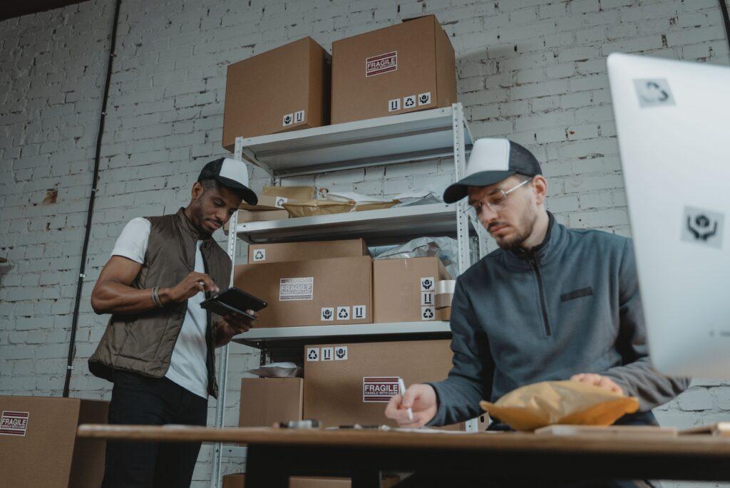 E-commerce warehouse employee managing international orders beside stacked parcels and a computer.